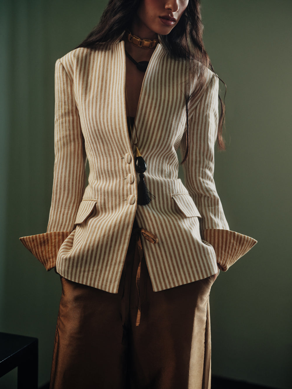 Front view of Daisy Cabane blazer showing beige-white stripes, tailored waist and fabric buttons on green background