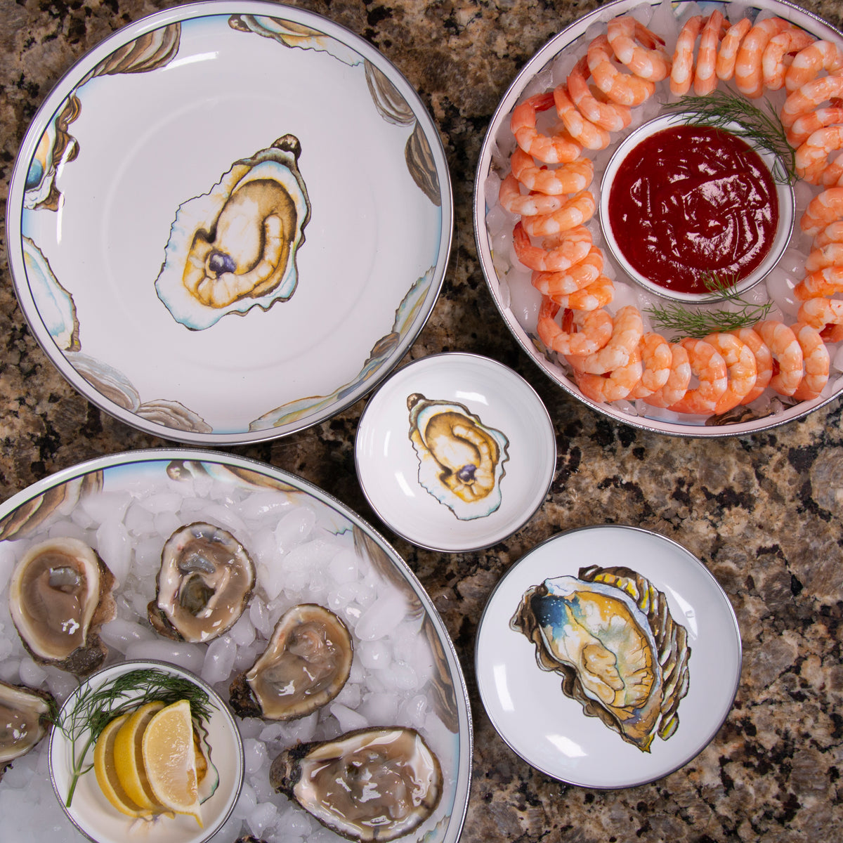 Oyster-themed serving dishes arranged with shrimp, oysters, sauce, and lemon on a countertop