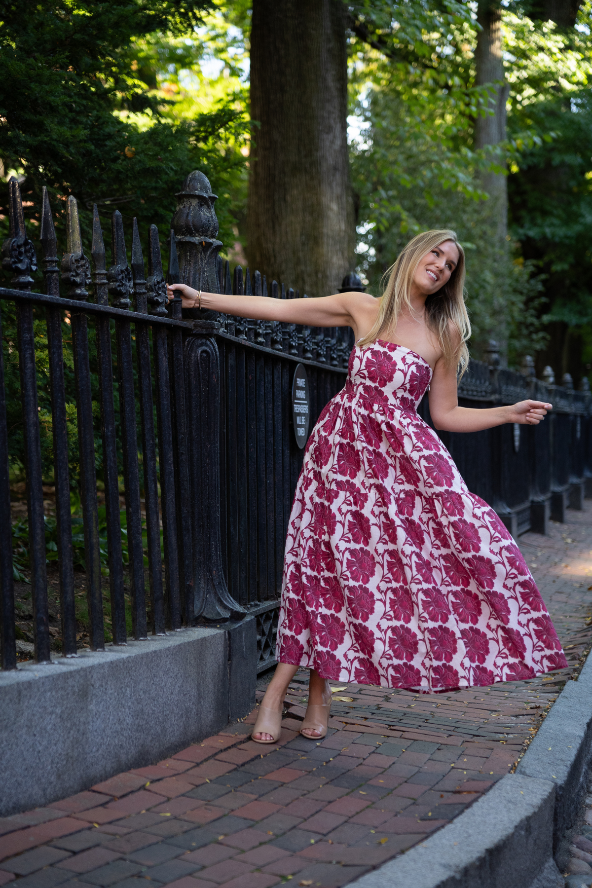 Three-quarter view of Barbie Dress in Dahlia showcasing straight-across bodice and floral mid-calf skirt by a garden fence