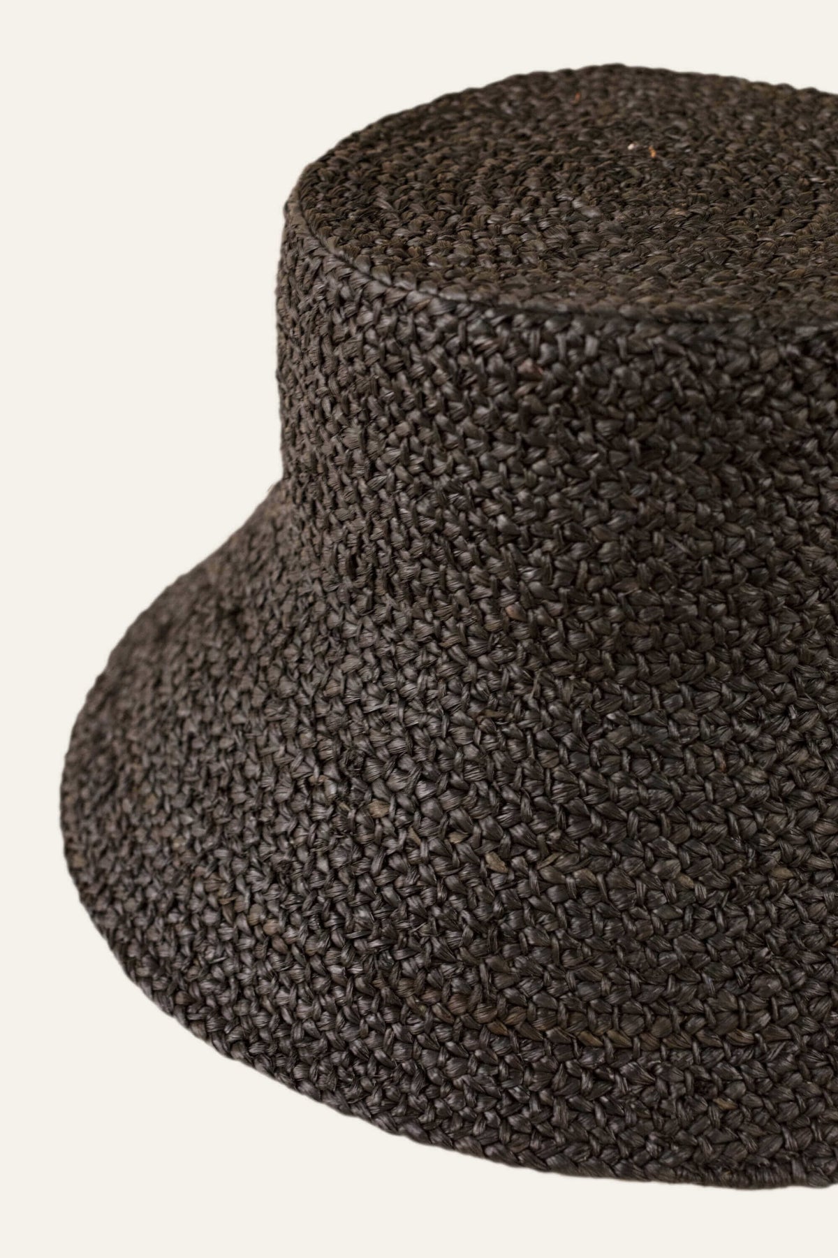 Close up side view of Raffia Bucket Hat in Black showcasing braided raffia texture and wide brim against a light background