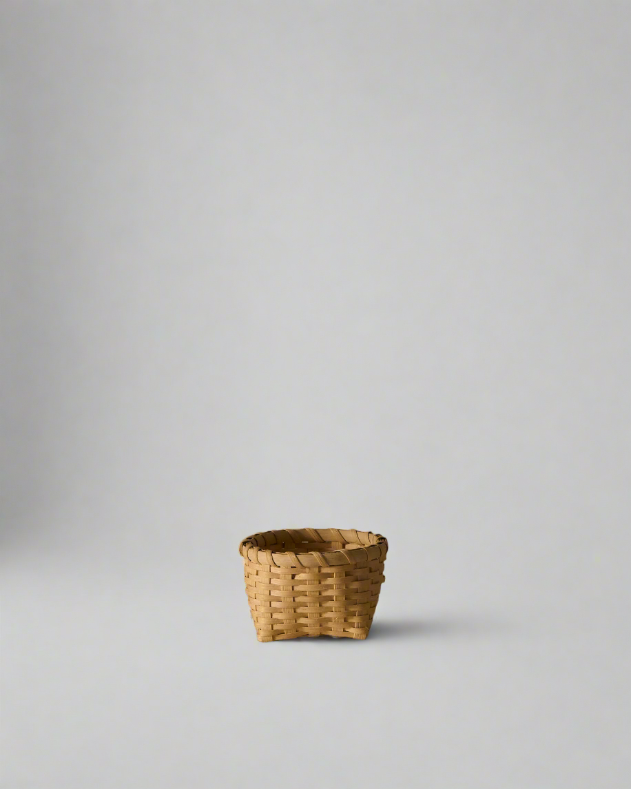 Front view of Little Love Basket showcasing woven natural rattan construction and rolled rim on light gray background