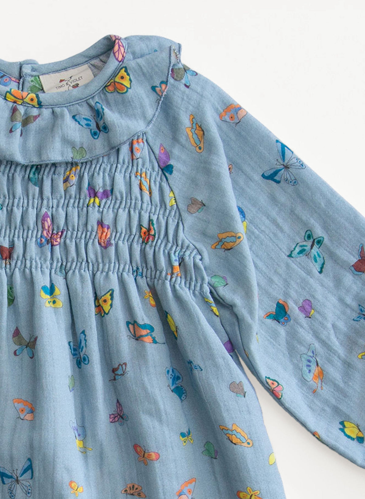 Close-up of The Gigi Dress in Blue Madame Butterfly showcasing smocked bodice and butterfly print on a white background