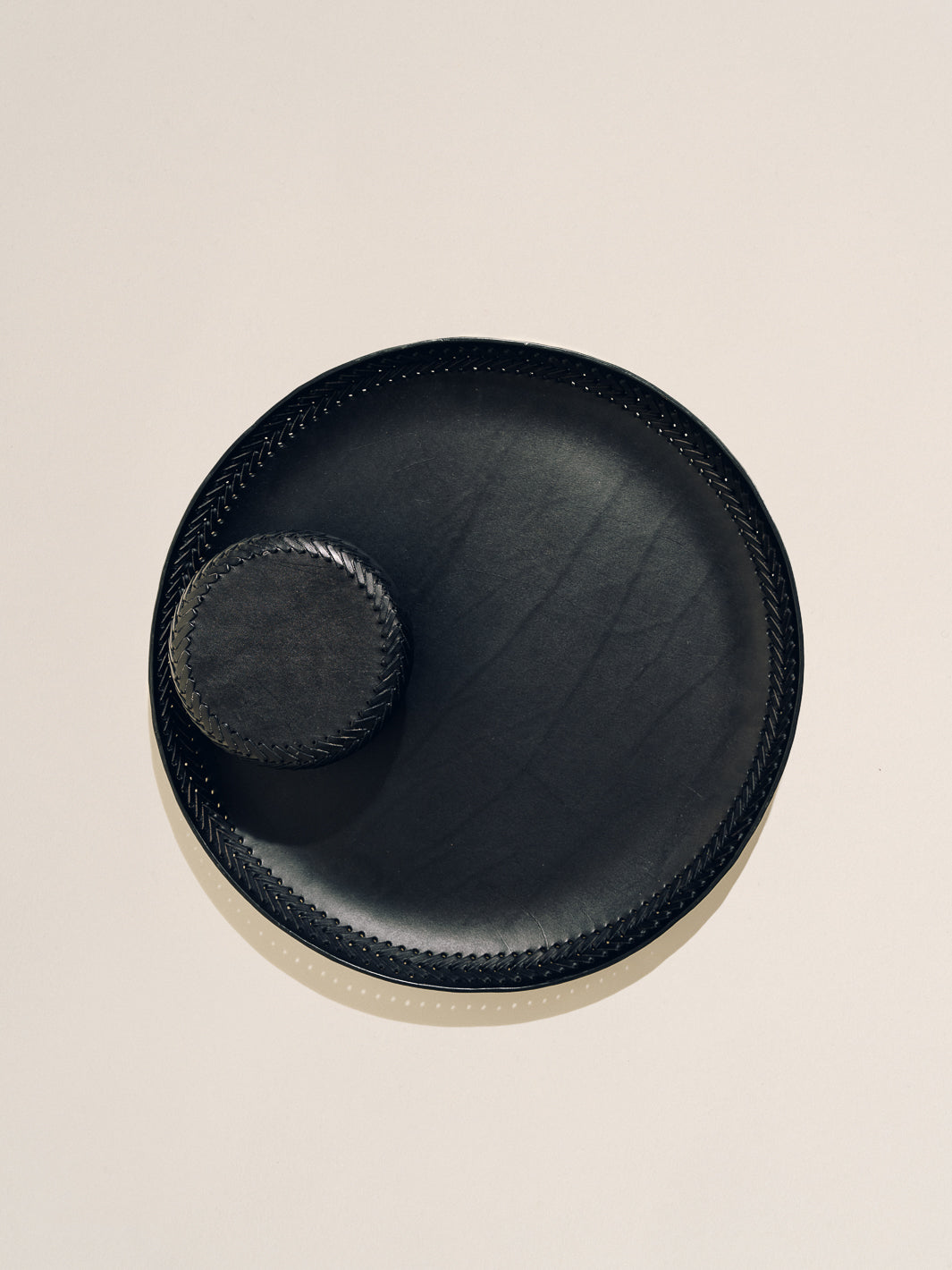 Top-down view of The Oversized Tray in black leather with woven lace trim and glossy hand-buffed finish on a cream background