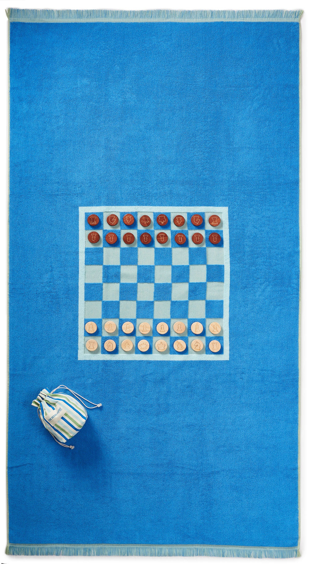Top-down view of The Montauk Beach Board towel with printed chess and checkers board, wooden pieces, and striped pouch on blue terry