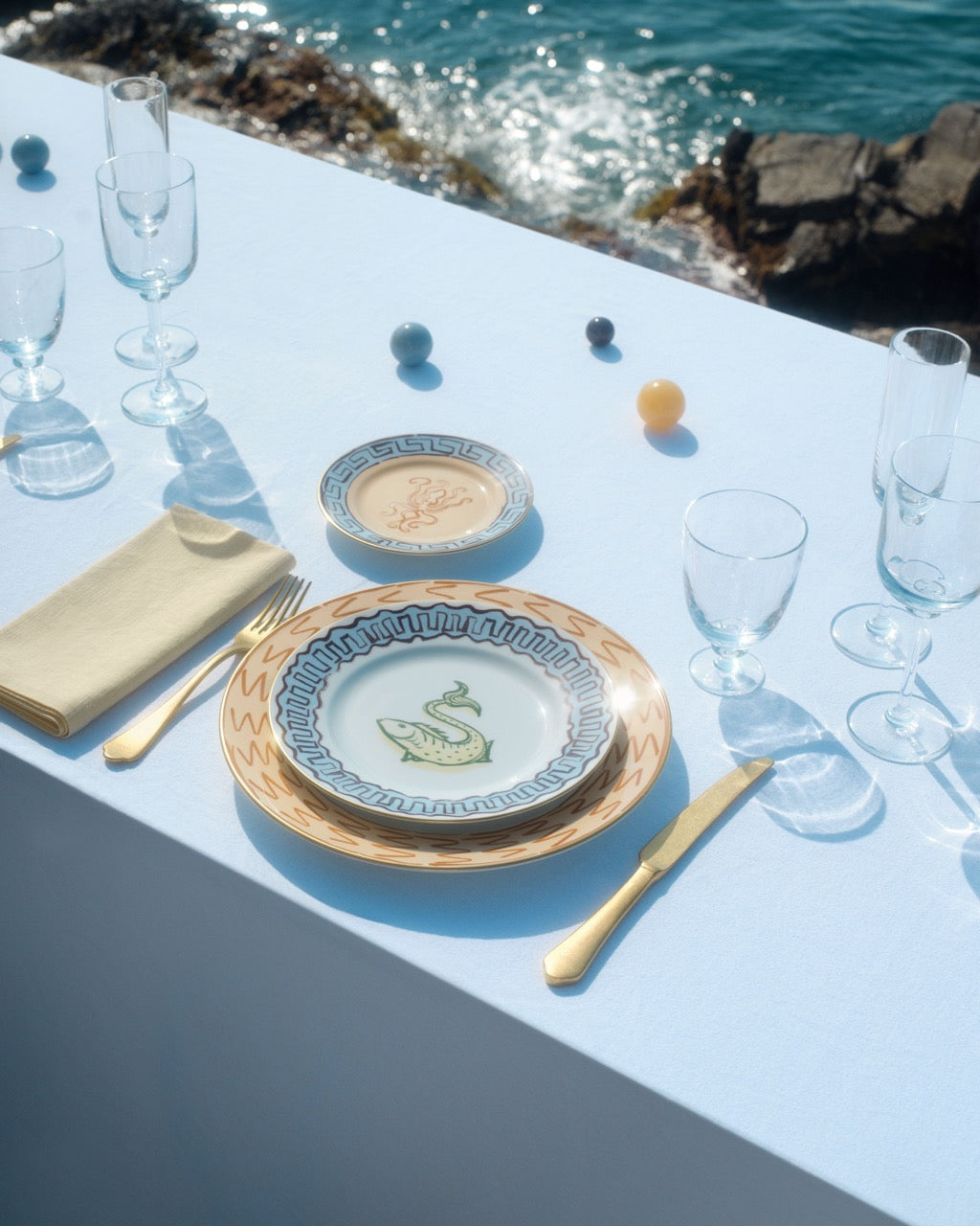 Top view of Ill Viaggio Di Nettuno dessert plate with Neptune fish motif and blue-and-yellow rim on pale blue table