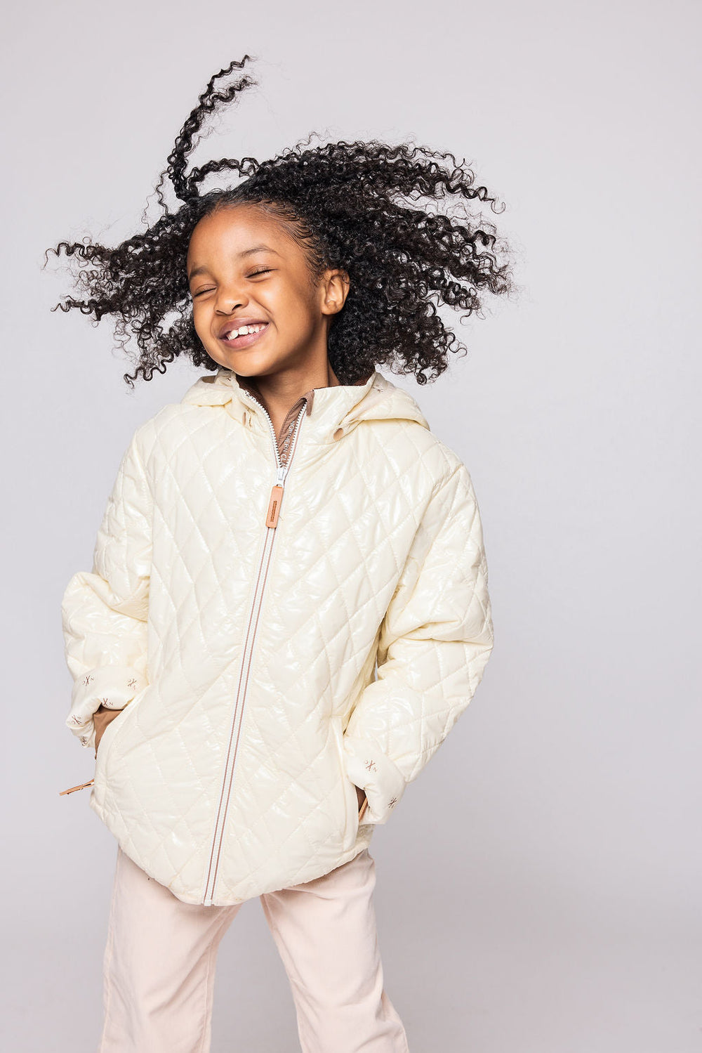 Front view of kids’ shiny white quilted puffer jacket on a smiling child showing diamond quilting, hood, front zipper, and pockets