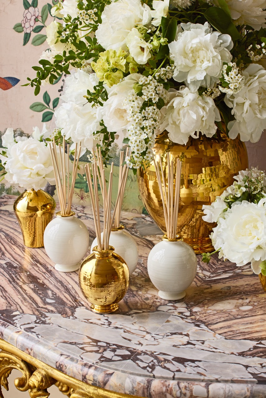 Front view of Siena Uzes Tuberose Diffuser Set showing cream and gold ribbed ceramic vessels with reeds on marble table