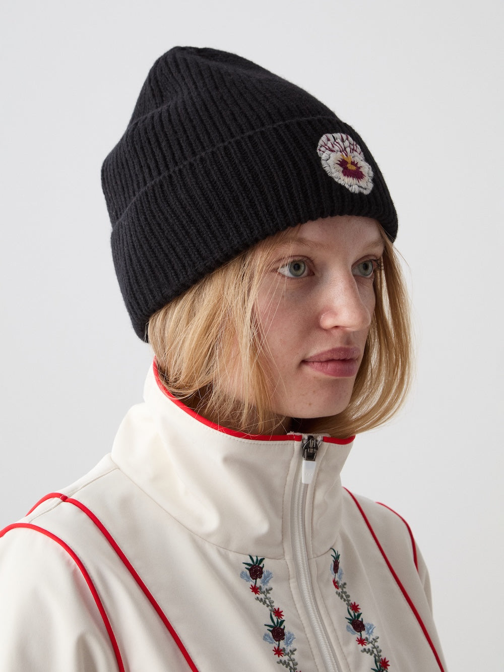 Three-quarter view of WN x Markarian Hat in Black showcasing embroidered signature flower with model against a light background