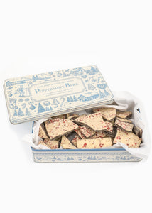 Open view of Tuck Shop for Over The Moon Peppermint Bark showcasing peppermint-topped chocolate pieces in a keepsake tin on a white background