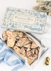 Top view of Over The Moon peppermint bark in a keepsake tin with peppermint-topped pieces, greenery, and ribbon