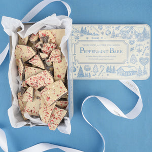 Overhead view of Over The Moon peppermint bark pieces with peppermint topping and keepsake tin on blue