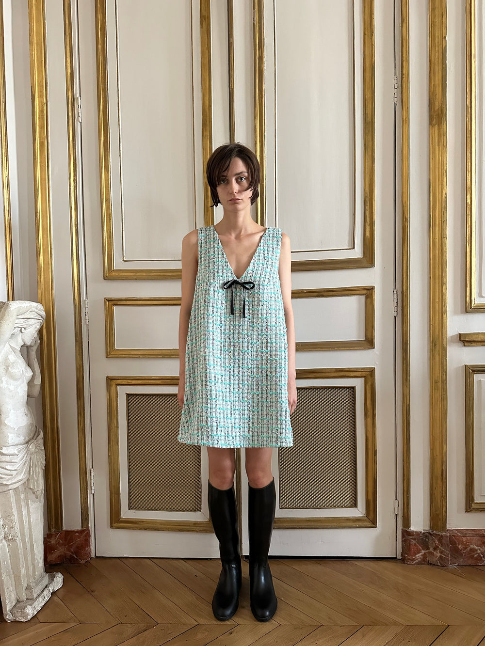 Front view of Liza dress in Verdure tweed showcasing V-neck and black grosgrain ribbon tie on a model against white and gold paneling