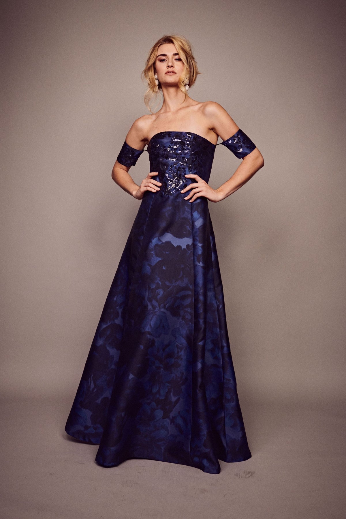 Front view of Vivien gown with strapless sequin bodice, armbands, and deep-blue floral skirt on neutral background