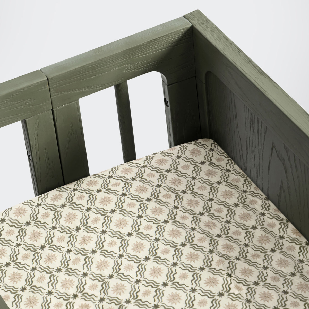 Angled view of All-Stages bassinet sheet in Juniper Star showcasing its repeating pattern on a dark green bassinet
