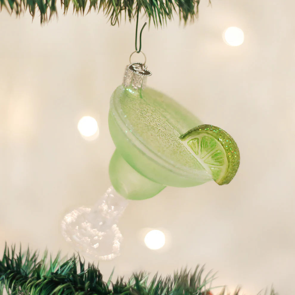 Angled view of margarita glass ornament with frosted green glass, glittered lime wedge, and salt-rim hanging from tree