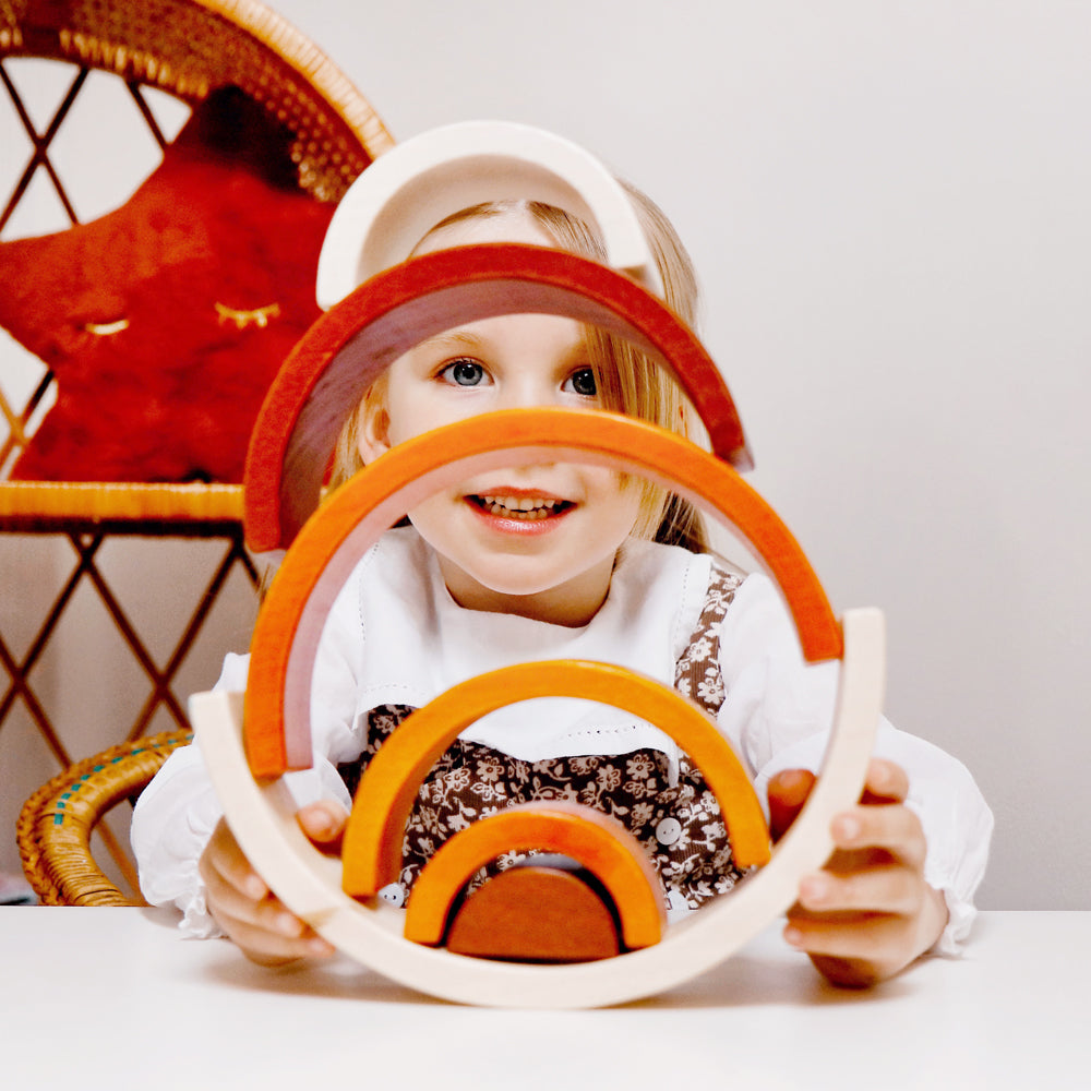 Child playing with a Natural Stacking Rainbow wooden stacking toy at a table