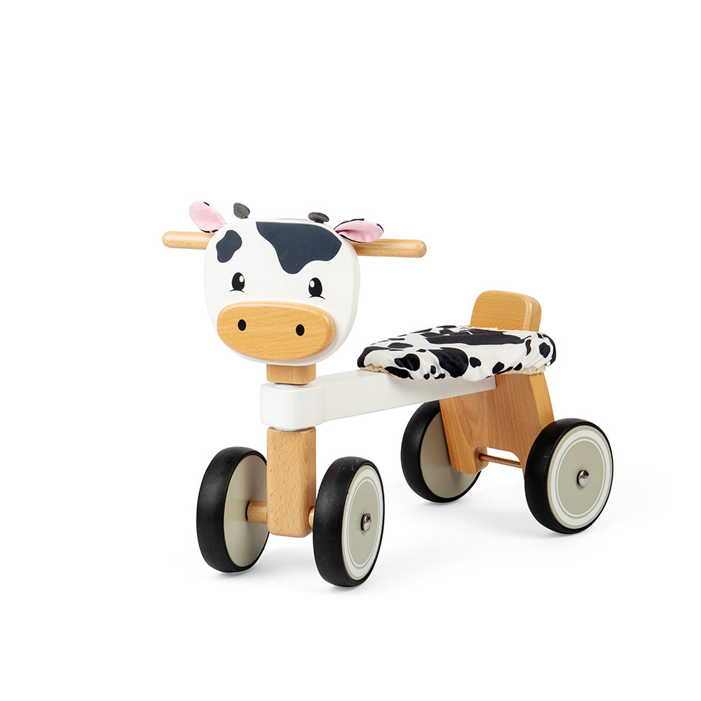 Front three-quarter view of Ride On Cow showcasing four wheels, wooden handlebars, and fluffy seat on a white background