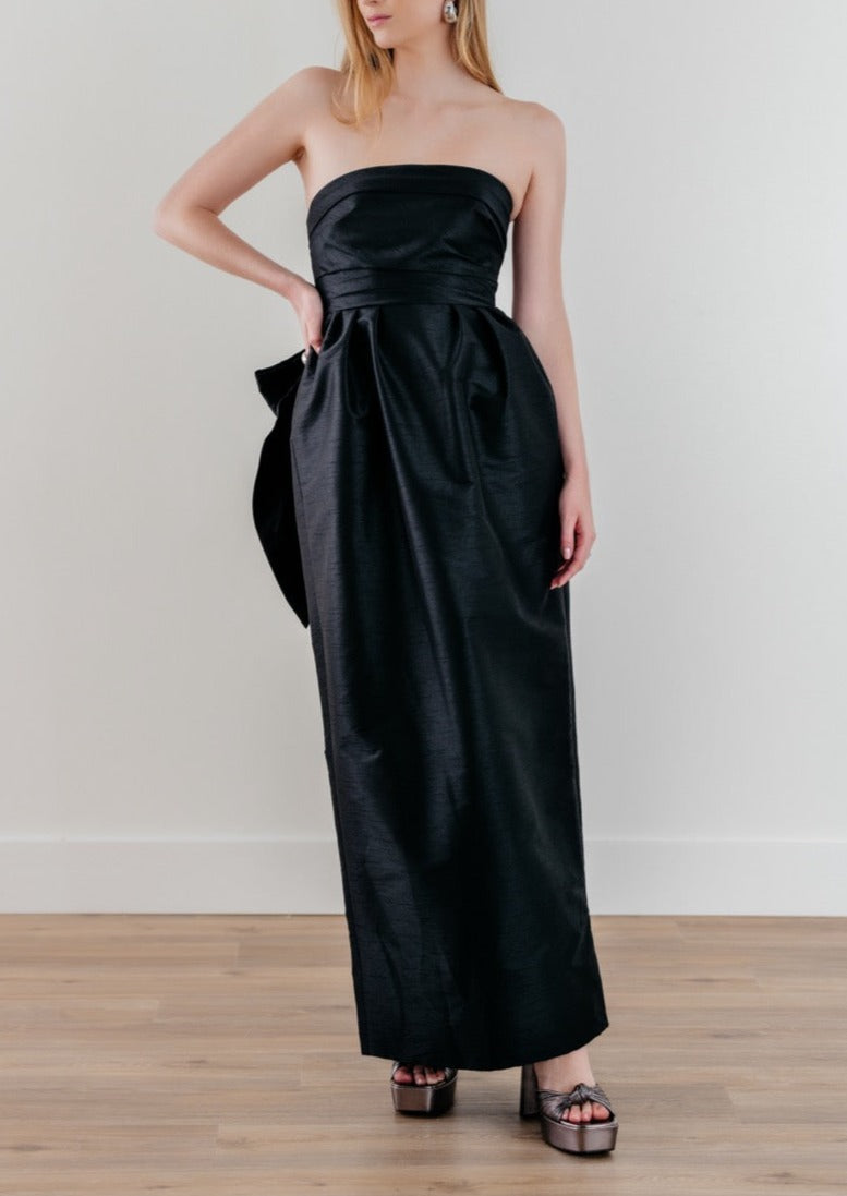 Front view of Caladium dress in black showcasing strapless bodice, long gathered skirt and side bow on light background