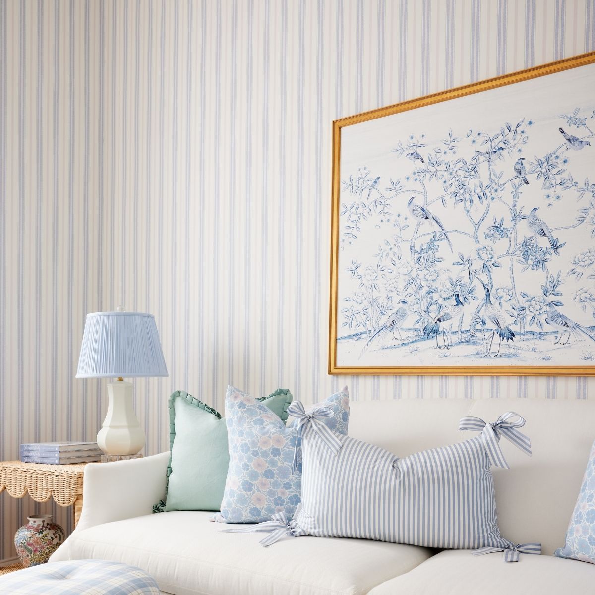 Styled living room showing Blue & Blush Halo Stripe wallpaper behind a white sofa with striped lumbar pillow and lamp