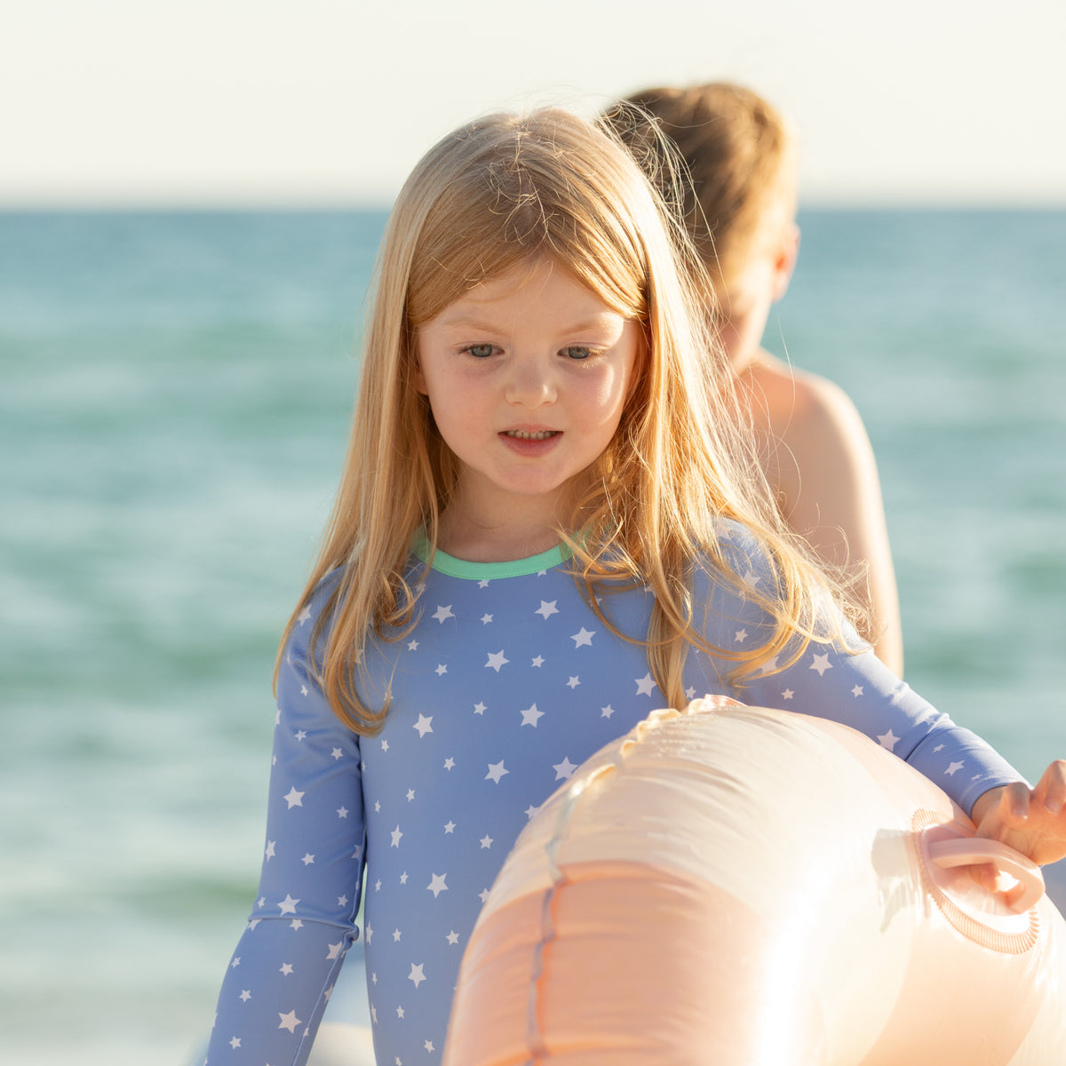 Girls’ long sleeve rashguard one piece swimsuit in Seaside Seersucker with UPF 50+ and scalloped open back, perfect for summer or beach vacations by Henry Duvall.
