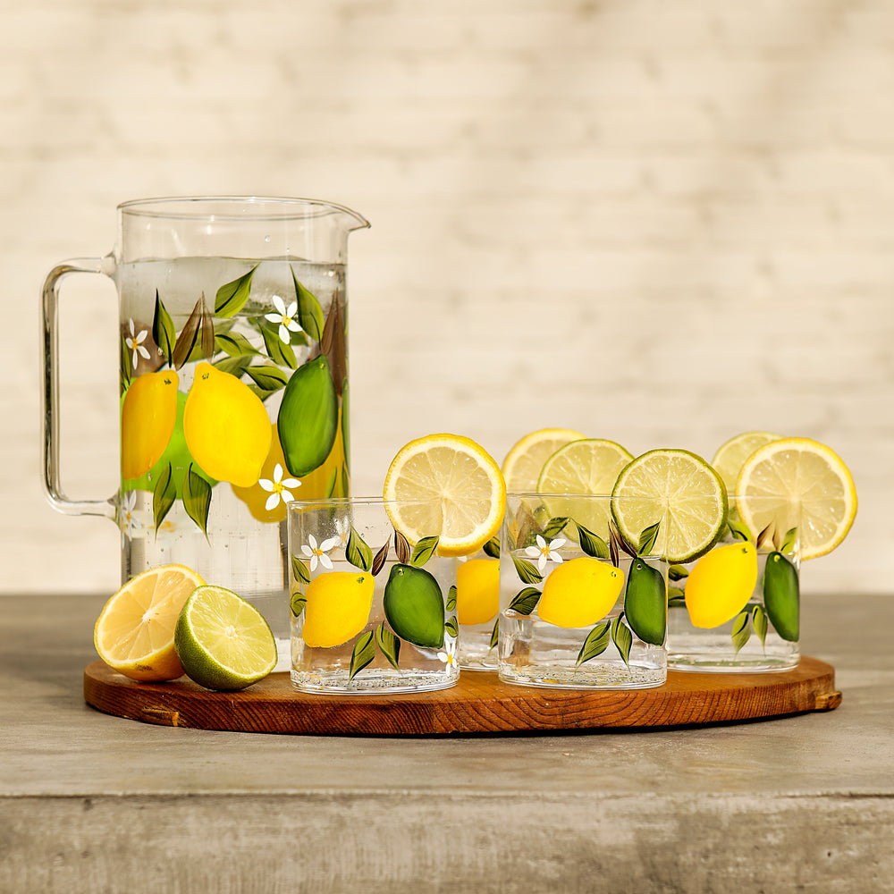 Front view of citrus jug with tumblers showing hand-painted lemon and lime motif on clear glass on wooden board
