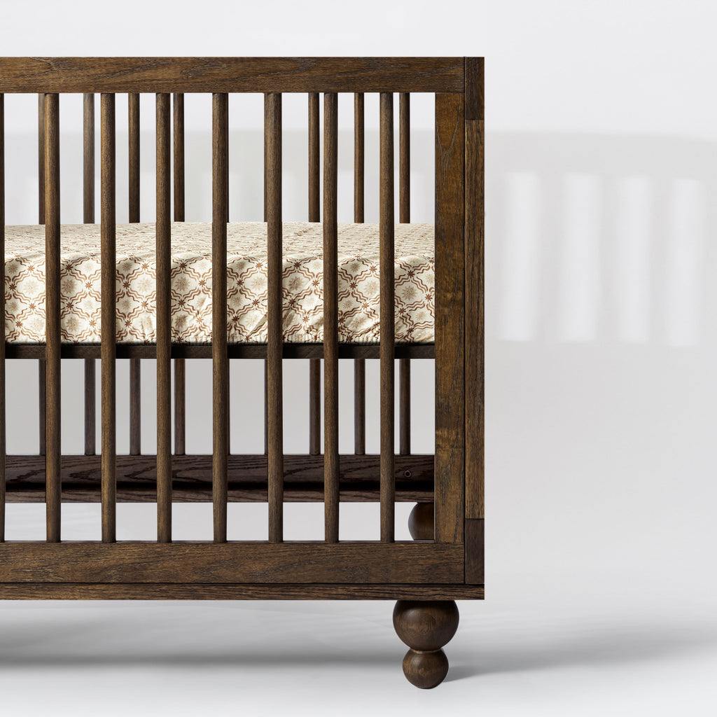 Side view of All-Stages Midi Crib Sheet in Autumn Star showcasing patterned cotton fabric on a dark wood crib