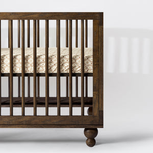 Side view of All-Stages Midi Crib Sheet in Autumn Star showcasing patterned cotton fabric on a dark wood crib