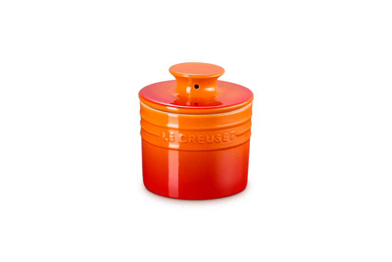Three-quarter view of Butter Crock 6 oz. in Flame showcasing its lid and embossed Le Creuset logo with a transparent background