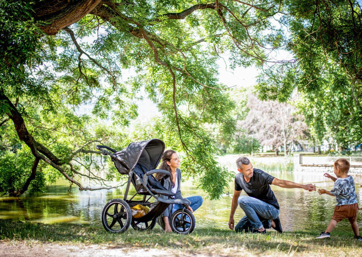 Family enjoying a lakeside park while a child walks beside the Runner 2 tricycle jogger stroller