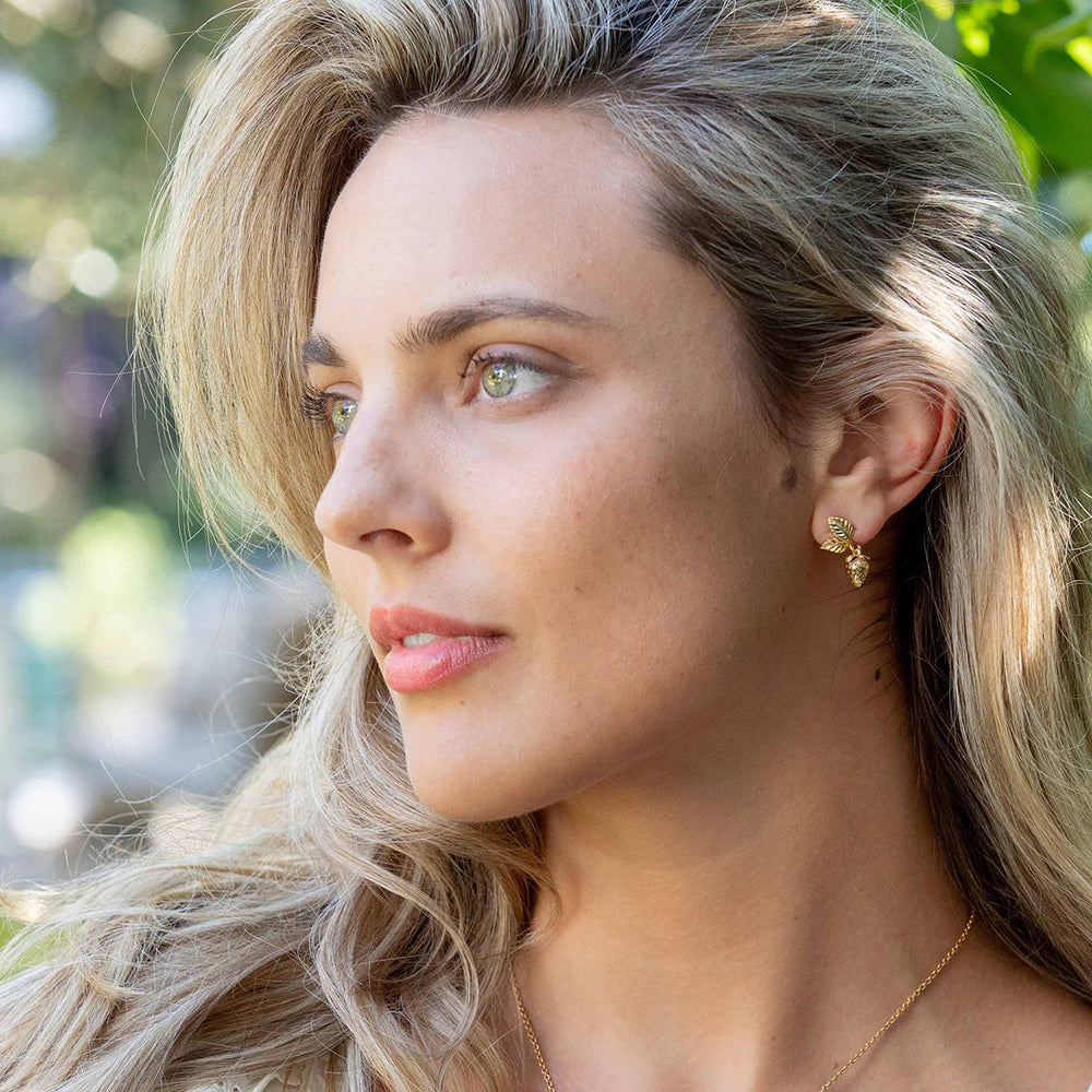 Close-up profile of Meadow Berry Drop Earrings in gold on a model showcasing textured golden berries and gilded leaves against blurred outdoor greenery