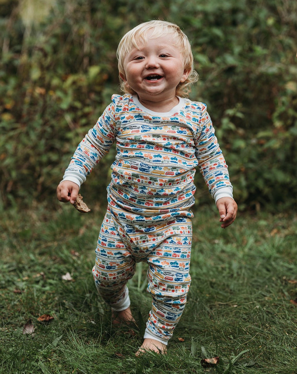 Front view of cars and trucks two-piece pajamas showcasing a colorful vehicle print on a smiling child outdoors