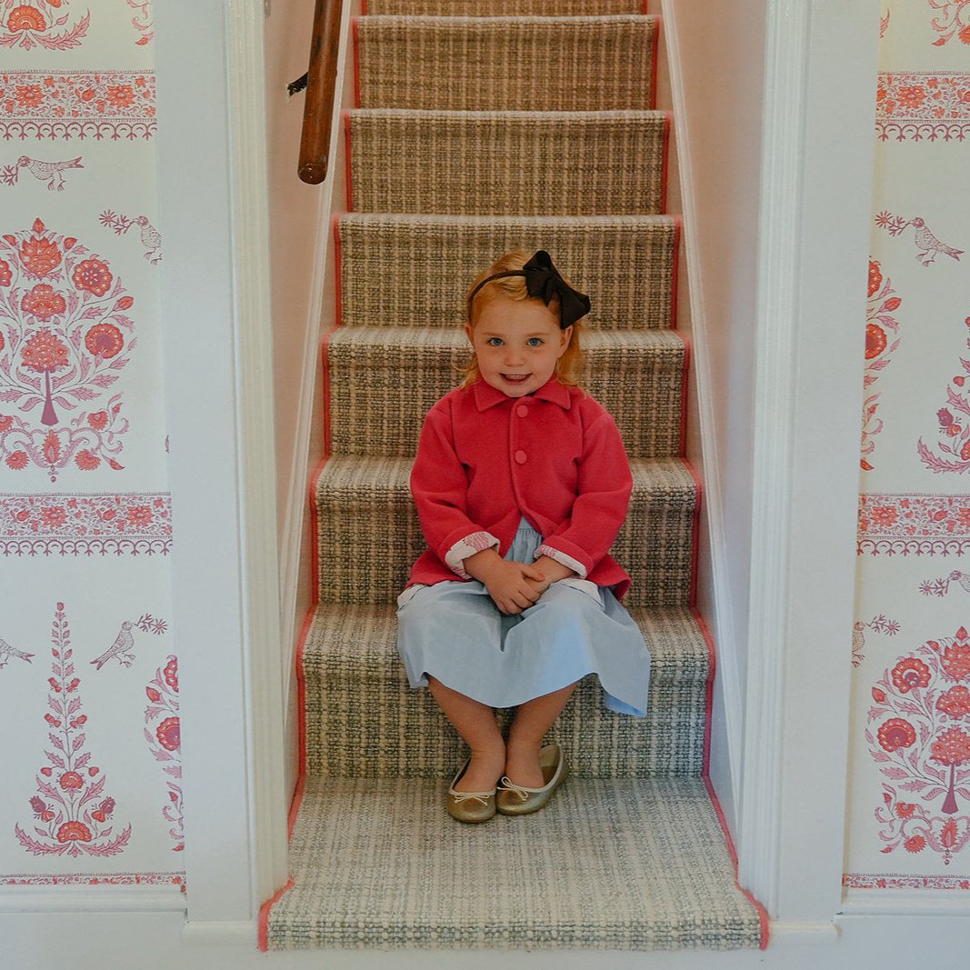 Front view of Children’s Perfect Layer Coat in pink on a toddler seated on carpeted stairs, showcasing button-front and collar