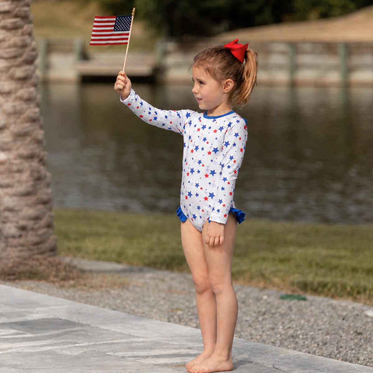 Henry Duvall Reese girls rashguard one piece in red white and blue star print, UPF 50+ long sleeve swimsuit for 4th of July, beach, and summer holidays