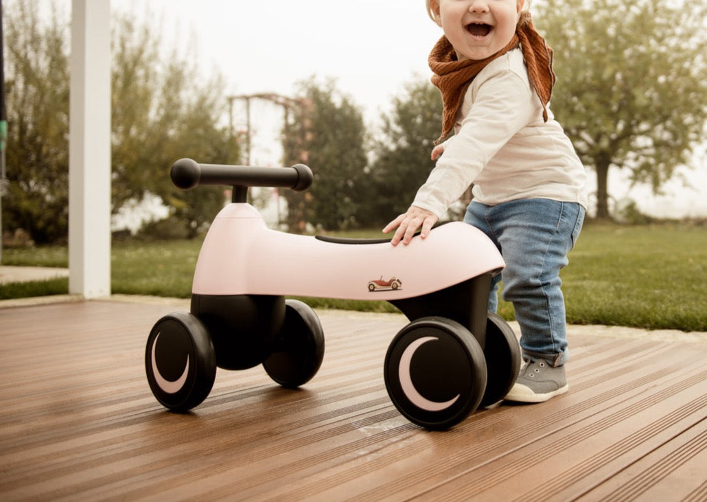 Toddler pushing pink 1st Ride Four ride-on toy on a wooden deck outdoors