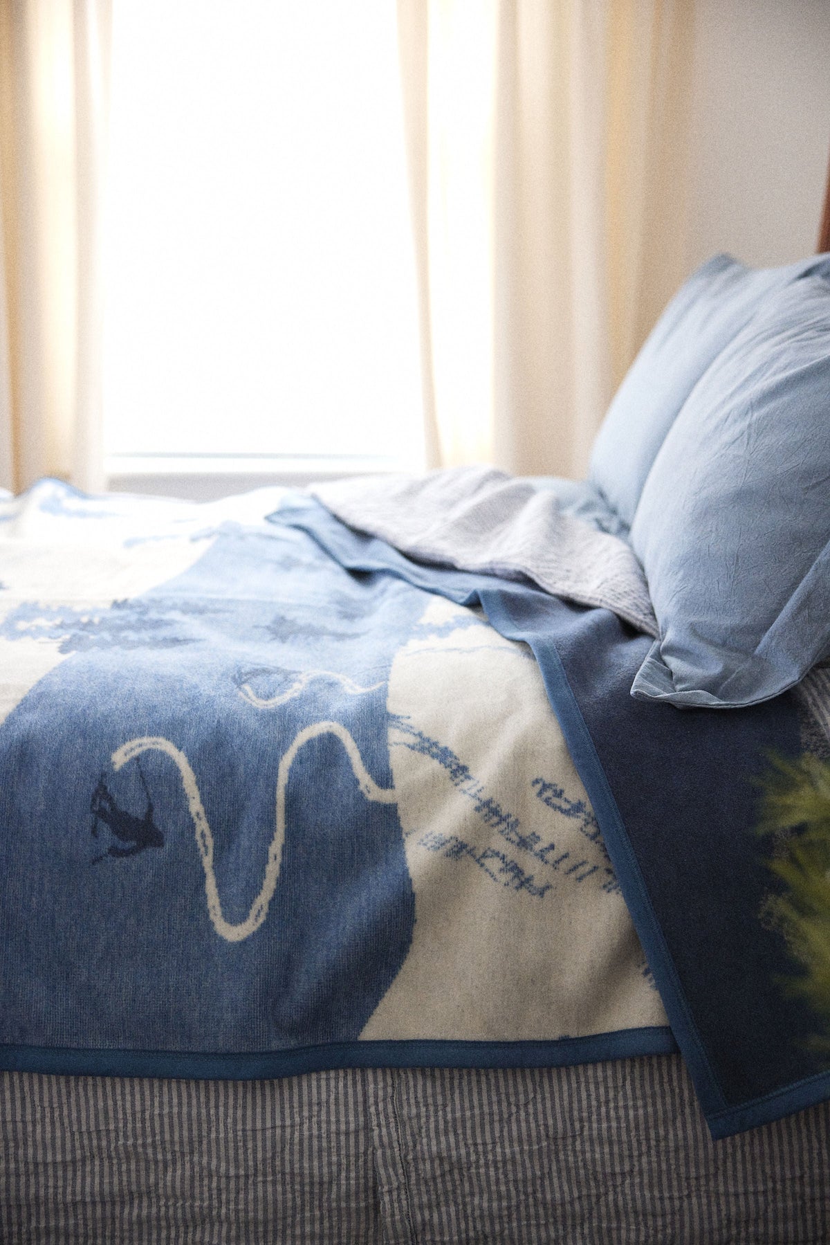 Blue and cream blanket with ski slope graphic draped over bed with pillows.