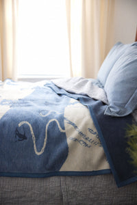 Blue and cream blanket with ski slope graphic draped over bed with pillows.