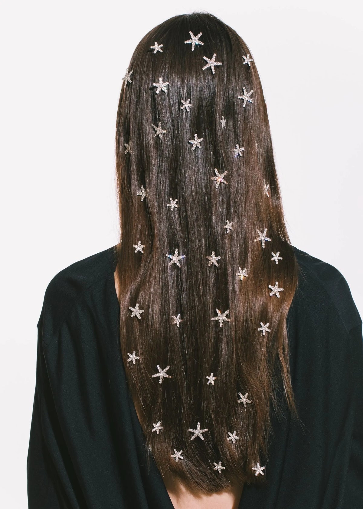 Rear view of Vespera Hair Magnets in crystal on long dark hair, star-shaped crystals scattered against white background