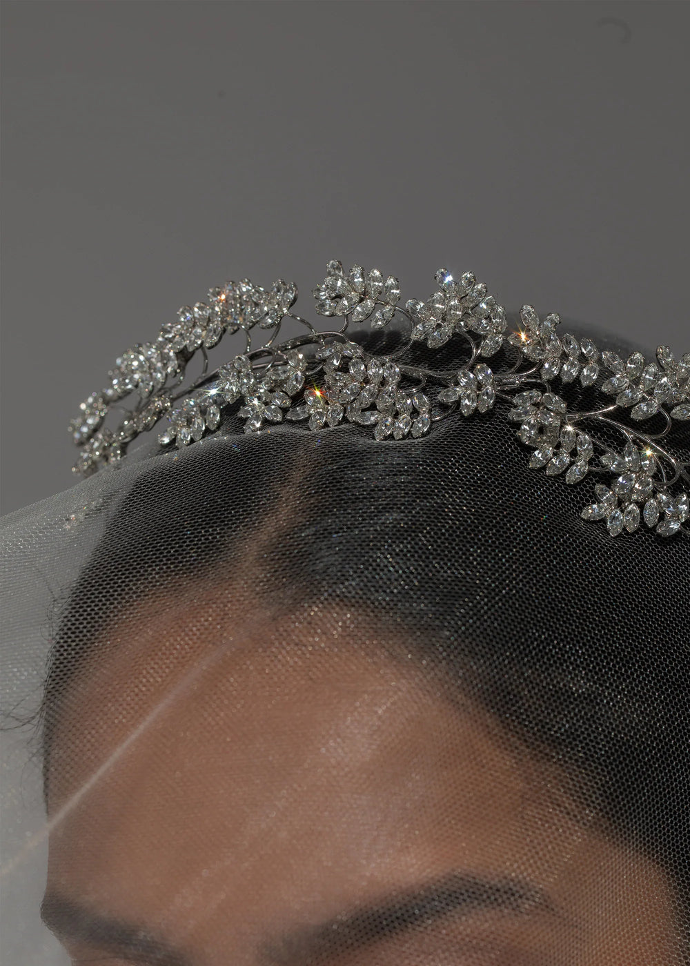 Close up of Raquel Tiara in Crystal showing clustered Austrian crystal leaf motifs on a rhodium plated vine-style base with bridal veil and neutral gray background