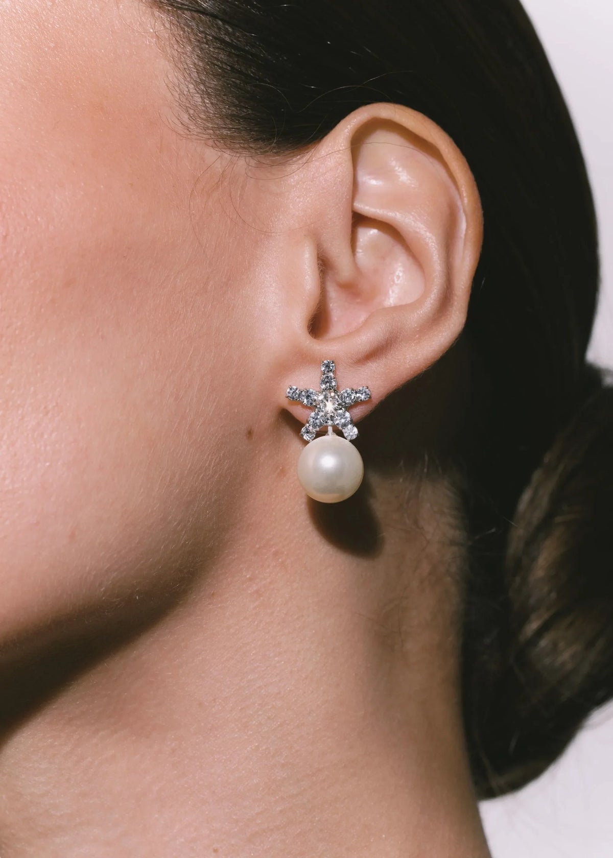 Close-up side view of Novella earrings in Crystal Pearl on model’s left ear showing star-shaped crystal studs with dangling pearl