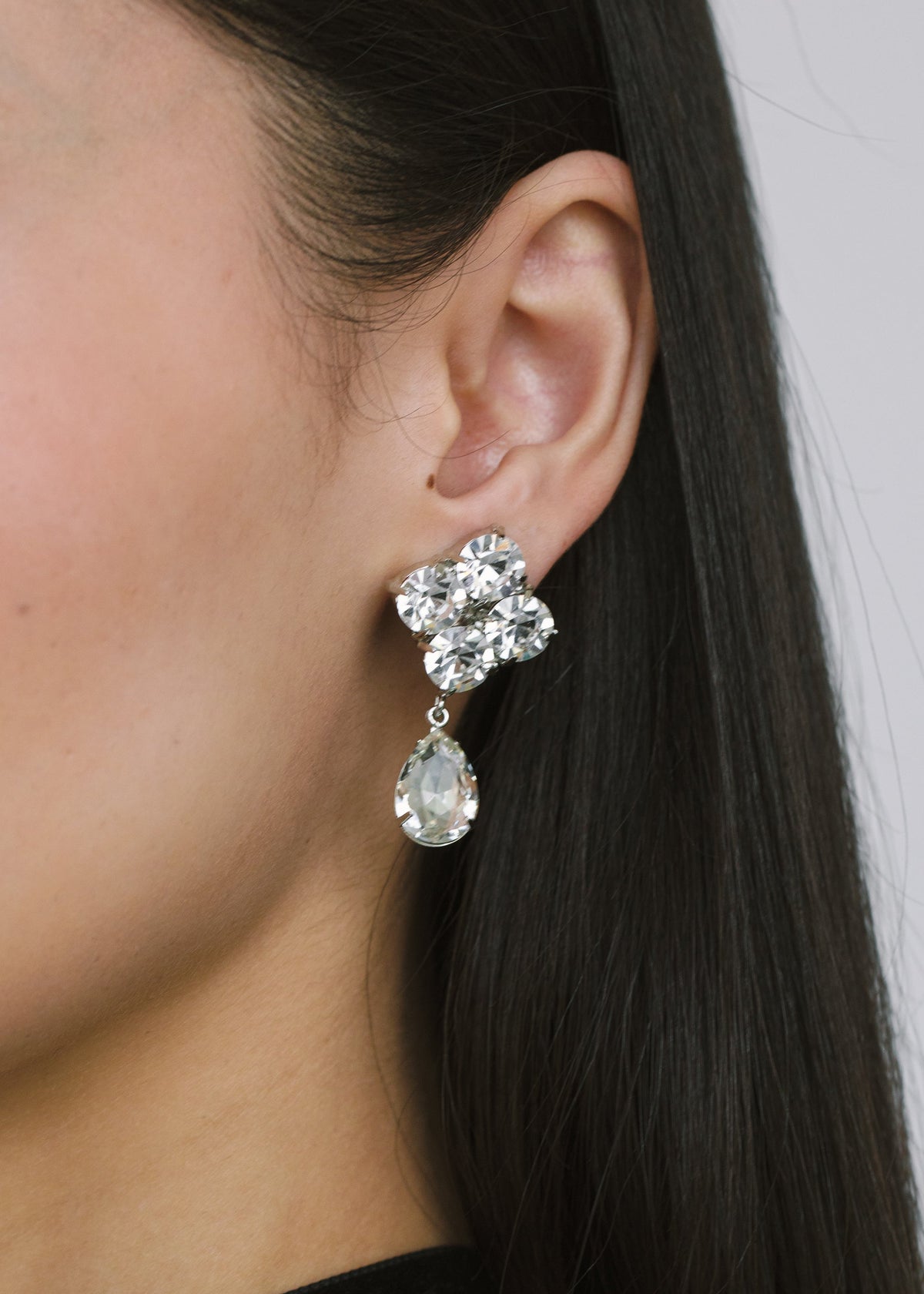 Close-up side view of Morgana Earrings in Crystal showcasing grouped faceted crystal stones and pear-cut drop on an ear