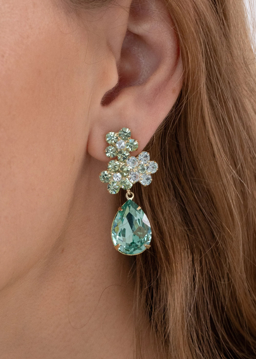 Close-up of Lauretta Earrings in Chrysolite showing floral crystal cluster and pear-shaped green drop on a model’s ear
