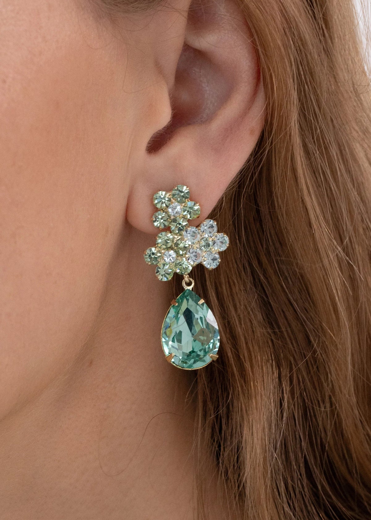 Close-up of Lauretta Earrings in Chrysolite showing floral crystal cluster and pear-shaped green drop on a model’s ear