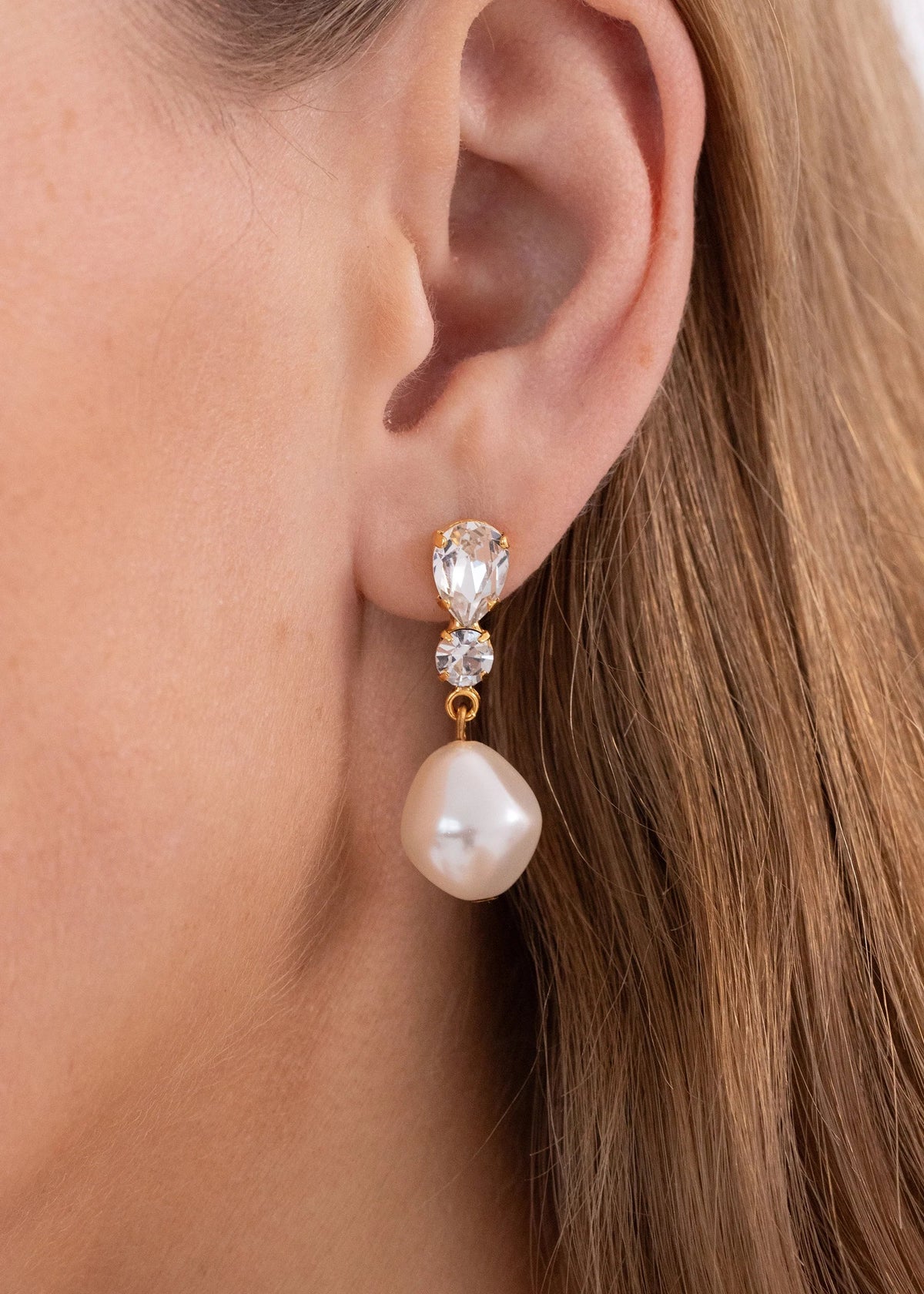Close-up of Kristina Earrings in crystal antique gold showing pear and round crystals with baroque pearl drop on ear