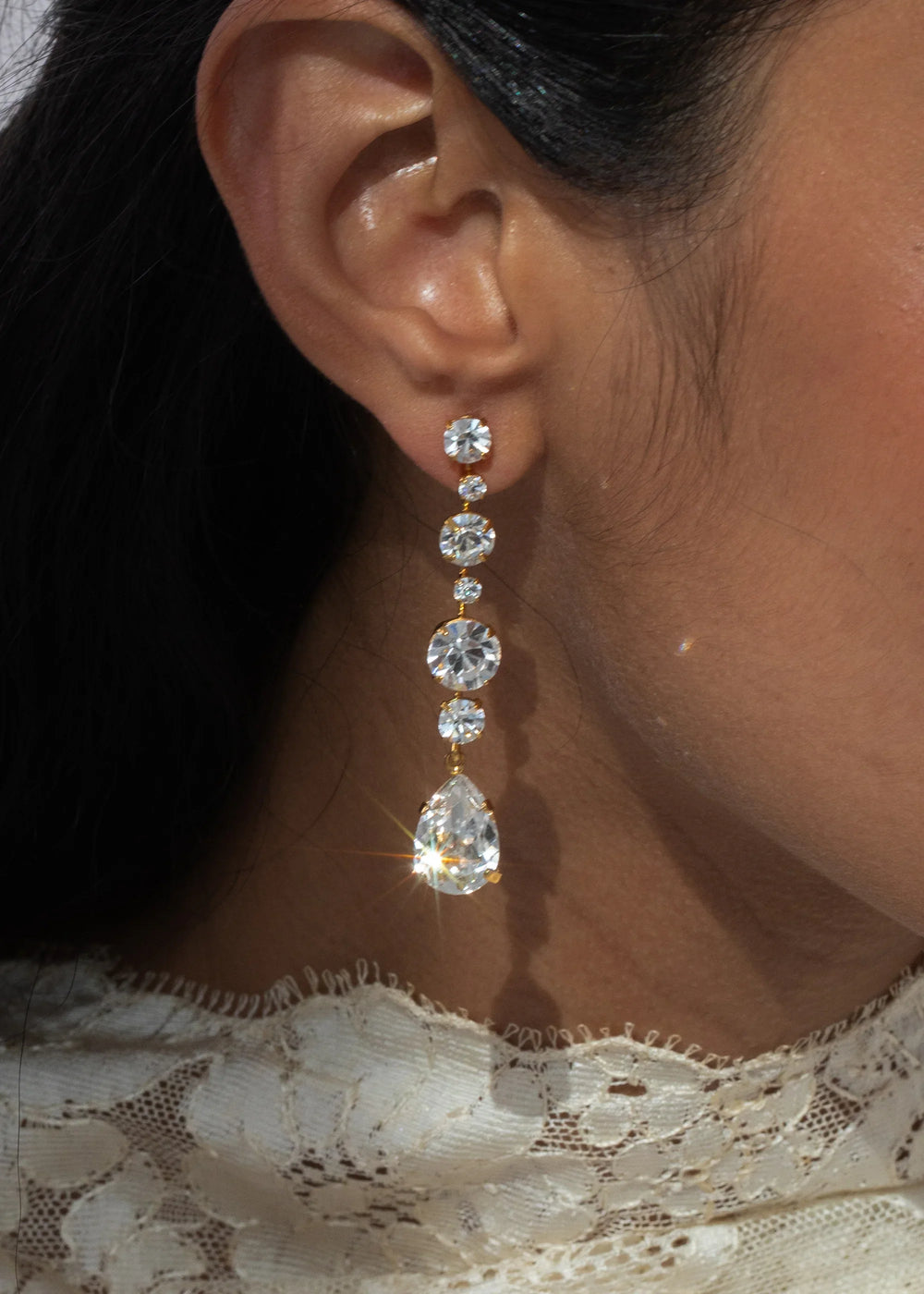 Close-up of Analia Earrings on model showcasing cascading oversized crystals ending in a pear-shaped drop in an antique gold setting
