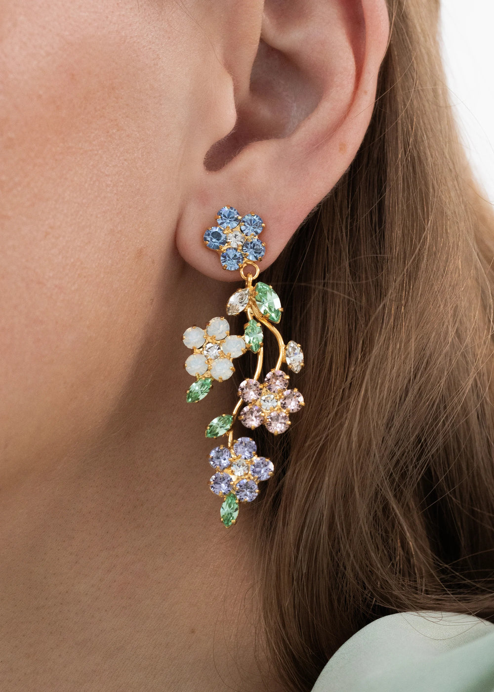 Close up of Adeline earrings in Garden showing cascading floral Austrian crystals and 18 karat gold plated branch on model’s ear