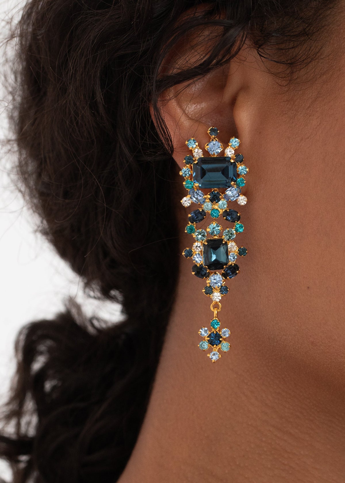 Close-up side view of the Candence Earrings in Sapphire showcasing emerald-cut blue crystals with dark hair background
