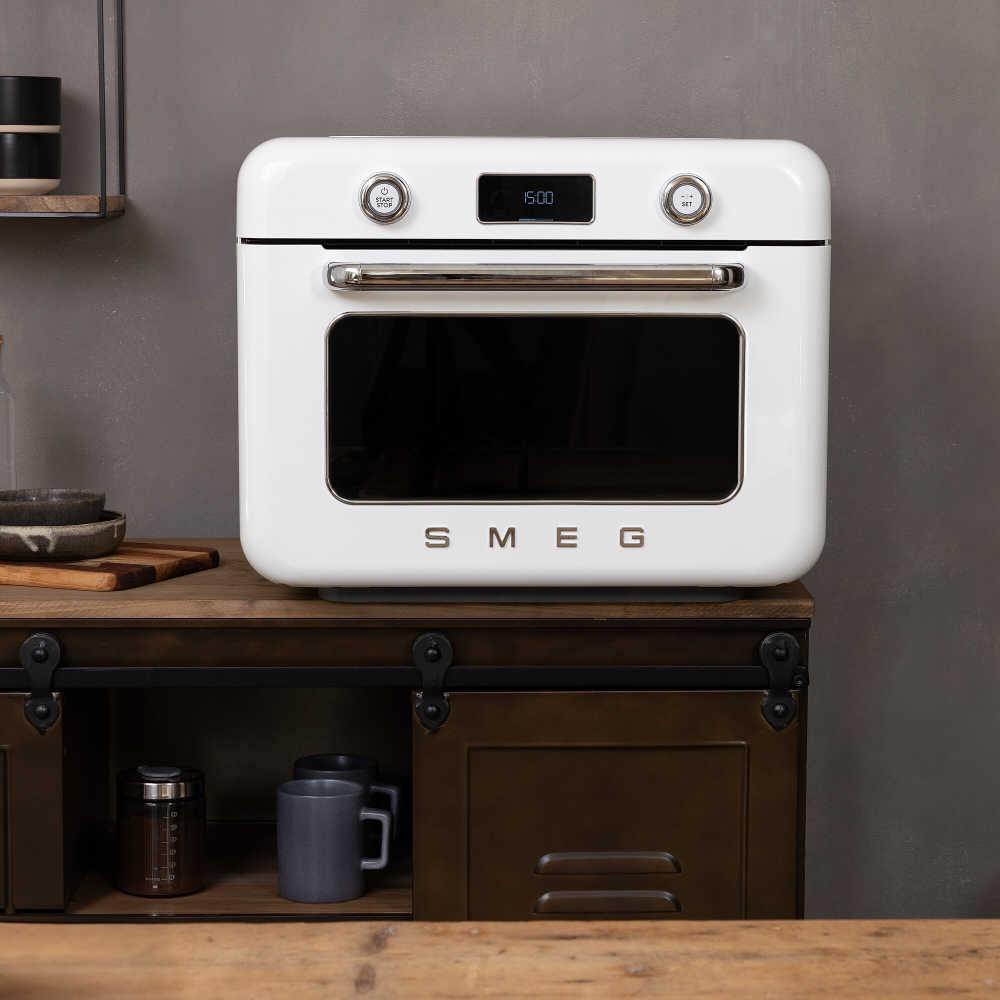 Front view of white Smeg combi oven with chrome handle, digital display, and black window on wooden cabinet