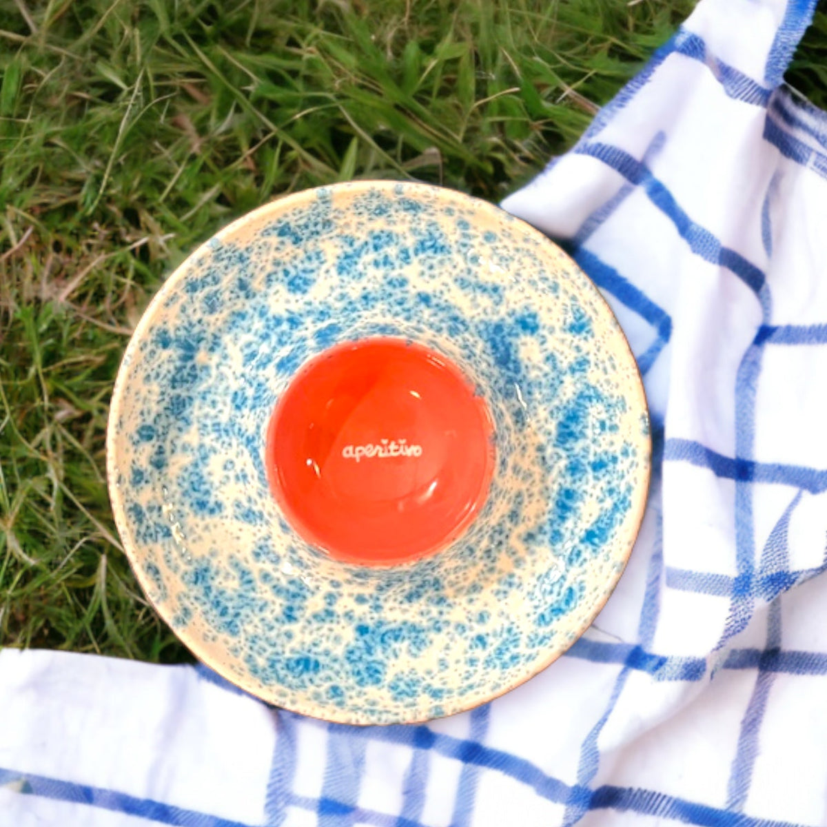 Top view of Hand-painted Aperitivo Platter showcasing blue and cream patterns with red center on grass and checked cloth