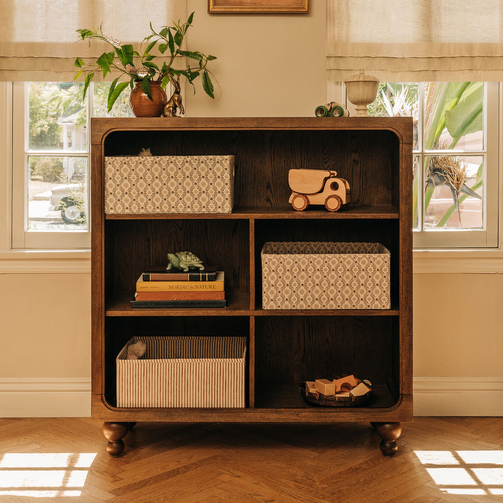 Front view of Astre Assembled Bookcase by Nate Berkus in Toffee with six compartments and rounded feet in a sunlit room