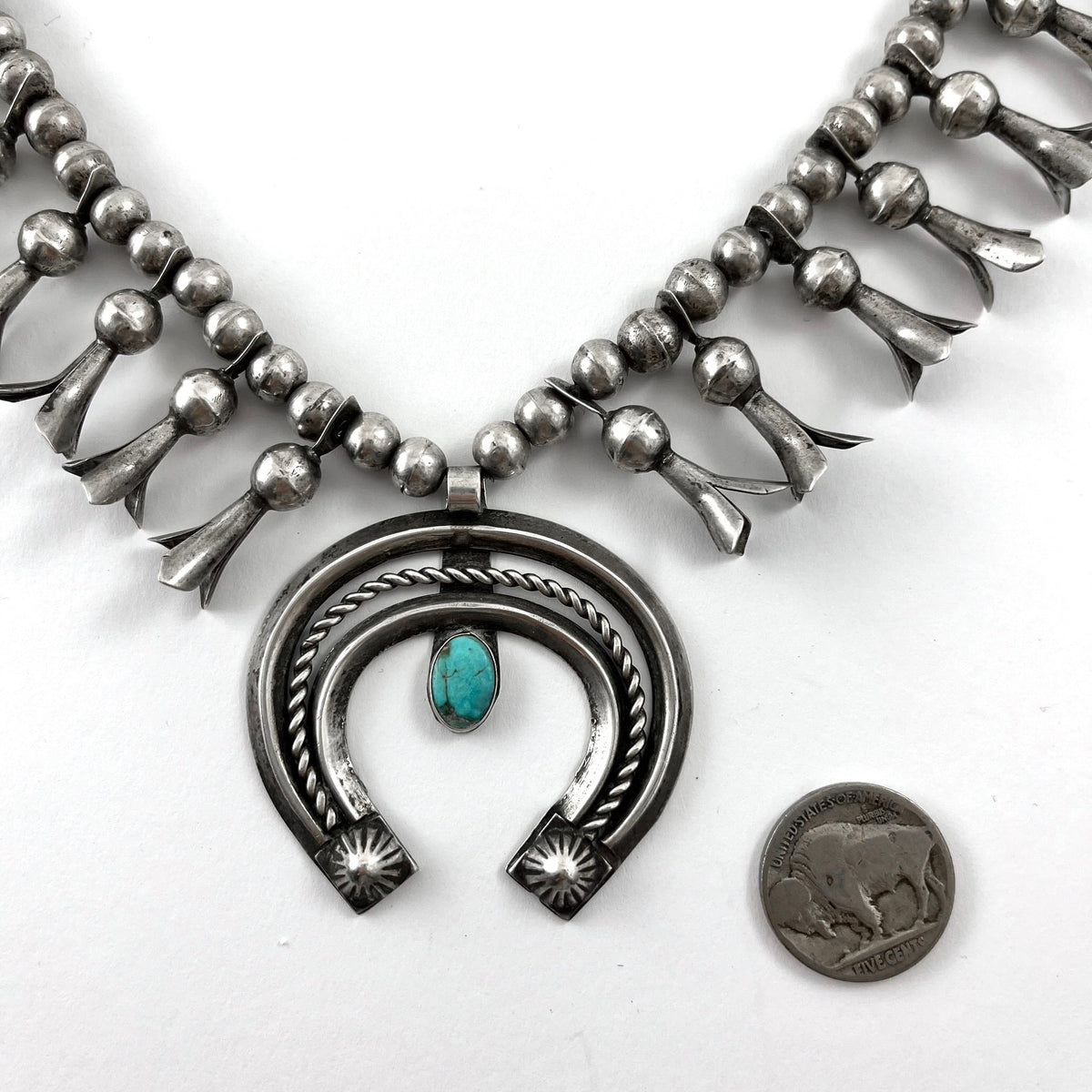 Close-up view of vintage sterling silver squash necklace showcasing turquoise naja and handmade silver beads on a white background